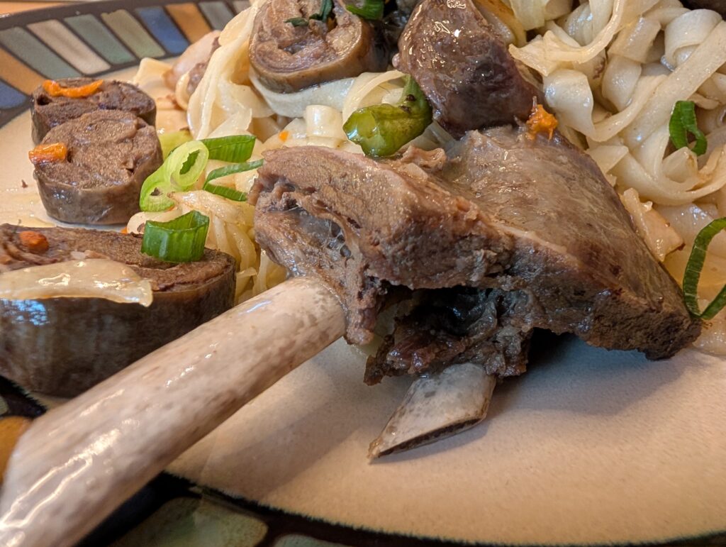 ツォイワンに乗った羊の骨付き肋肉と自家製ビーフソーセージのアップ